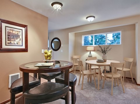 Dining area with a round table and chairs beside a separate seating nook under a wide clerestory window.