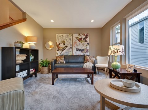 Living room with a sofa, armchair, bookshelf, coffee table, recessed ceiling lights, and two windows.