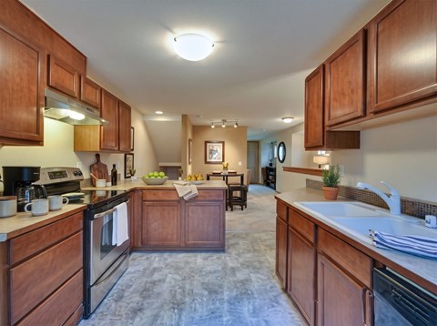 Galley kitchen with wood cabinets, stainless range, double sink, and a peninsula opening to the dining area.