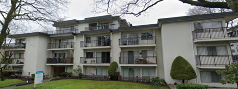 Apartment building with balconies and greenery in front.