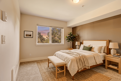 A bedroom with a large bed and a window overlooking a forest.