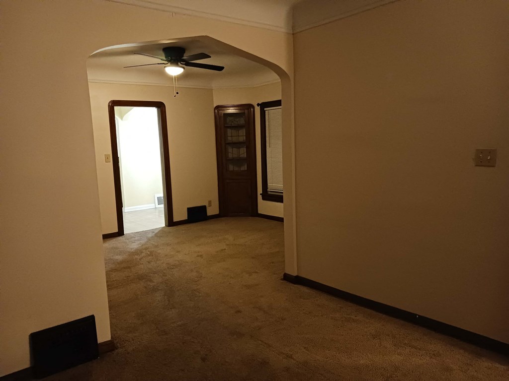 an empty living room with a ceiling fan and a door to a hallway