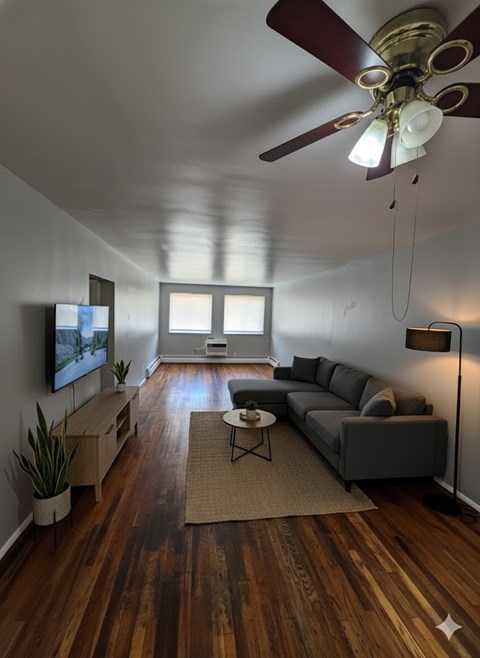 A living room with a grey couch, a coffee table, a television, and a ceiling fan.