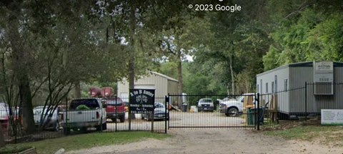 A black sign with white text is on a gate in front of a building.