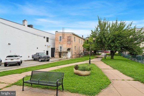 A green bench sits on a sidewalk next to a tree and a planter.