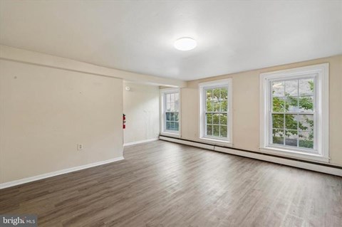 A spacious room with wooden flooring and two windows.