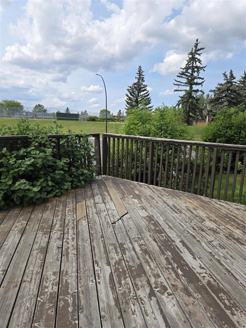 A wooden deck with a view of a grassy field and trees.
