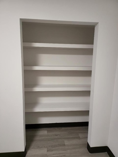 a walk in closet with white shelves and a wood floor