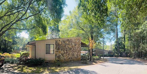 A small house with a stone wall is surrounded by trees.