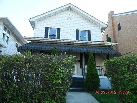 A white house with a black awning and a small tree in front.