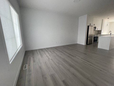 an empty living room with wood flooring and a kitchen