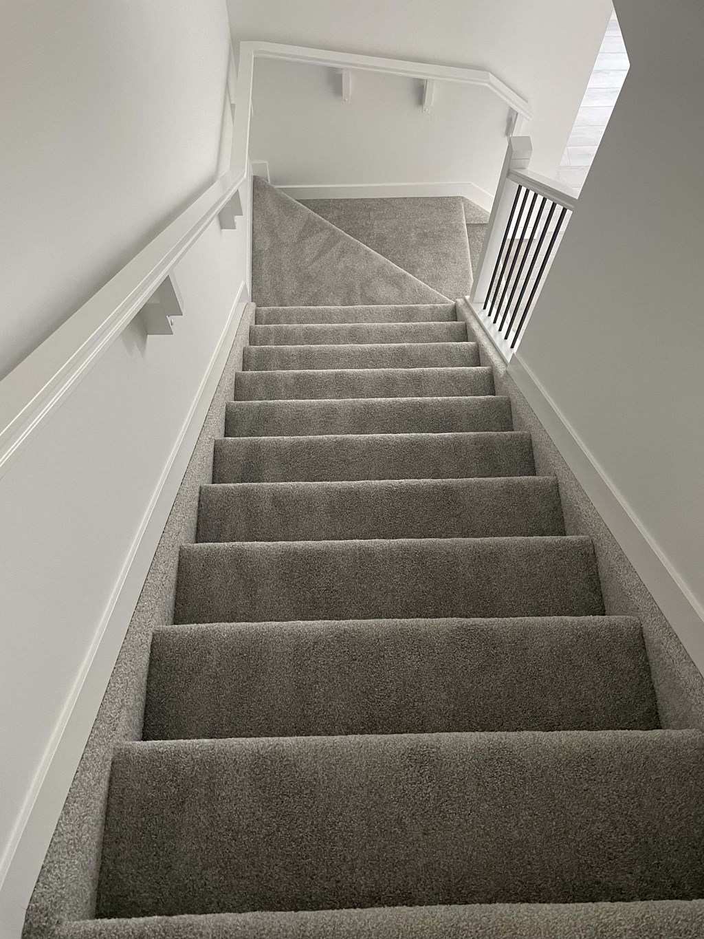 a gray carpeted staircase in a house with white walls and a white railing with
