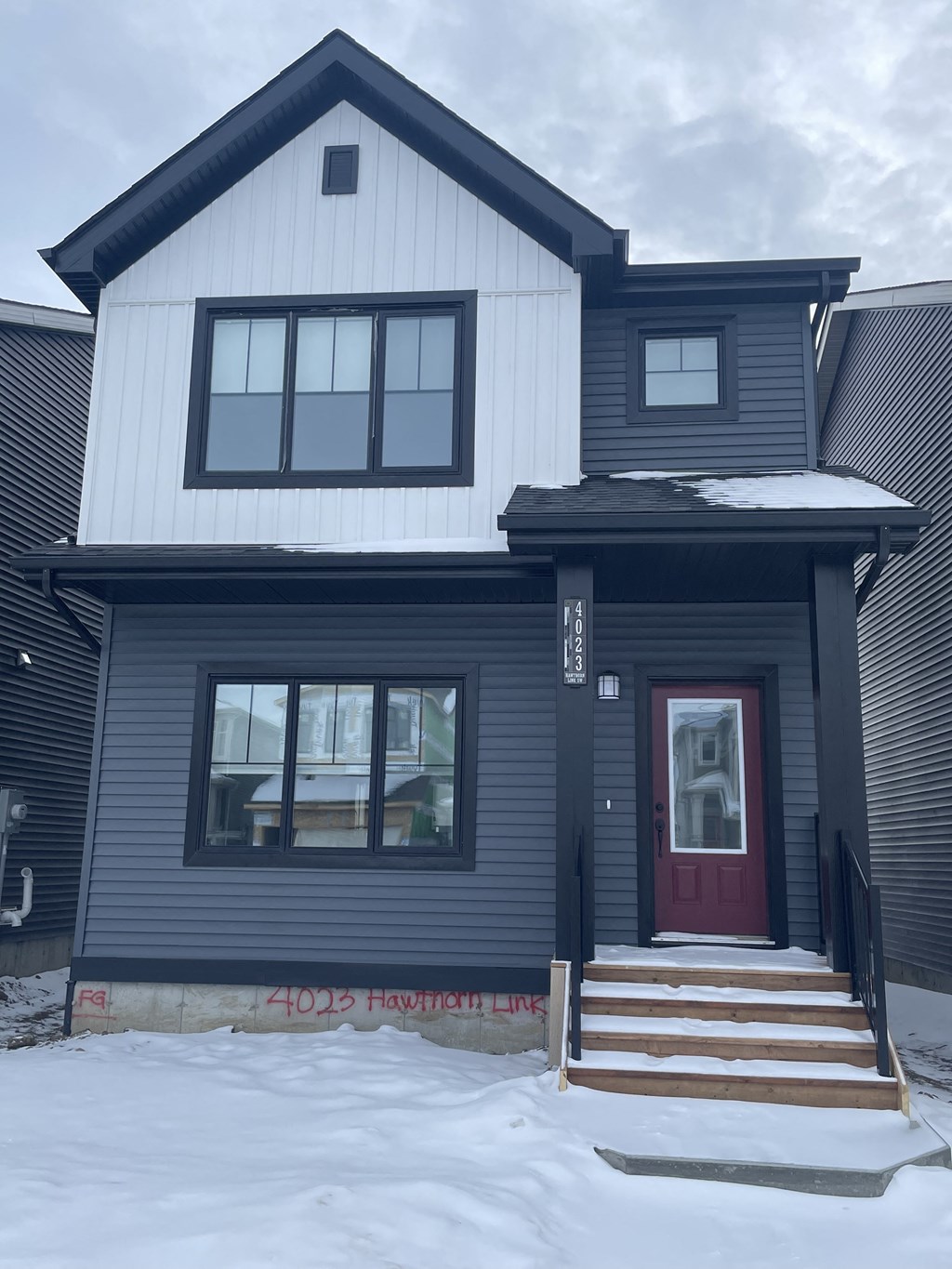a black house with white siding and a red door