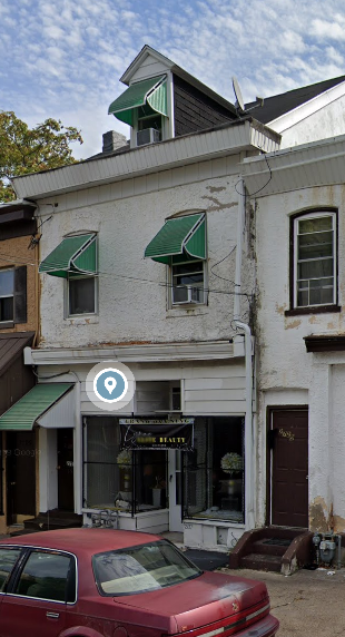 A red car is parked in front of a white building with a green awning.