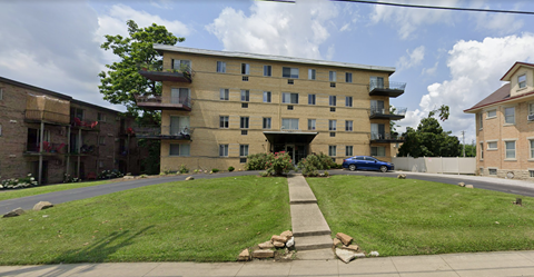 the exterior of an apartment building with a lawn and a blue car