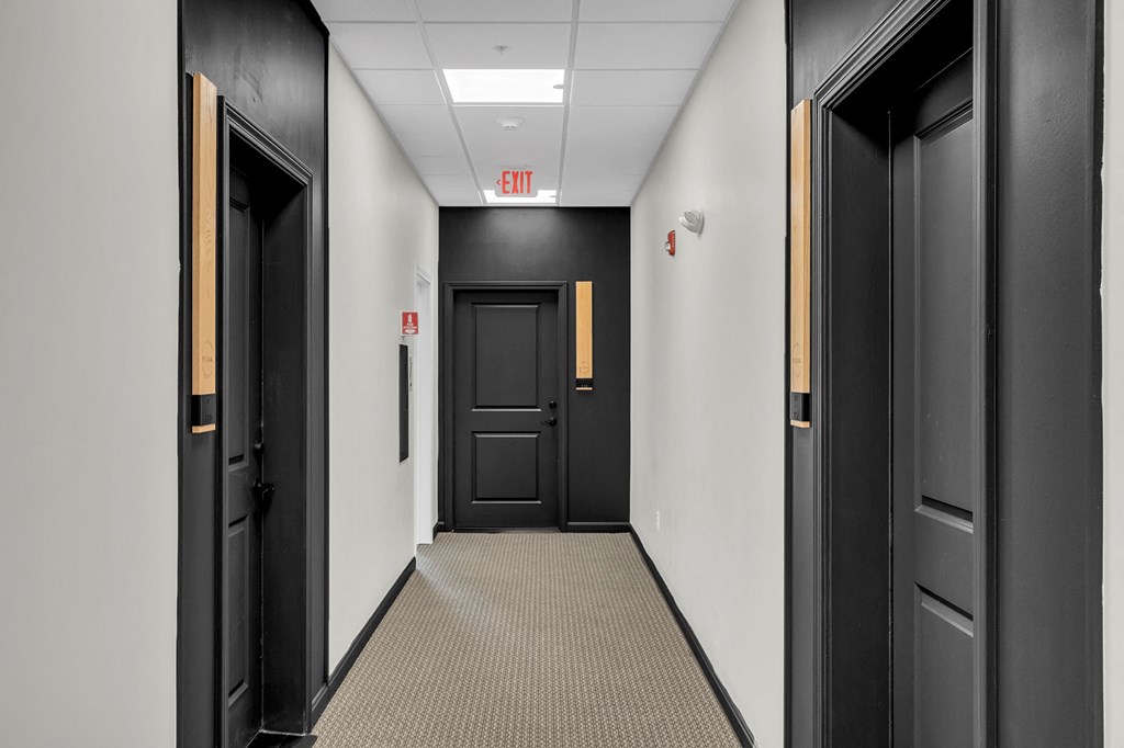a hallway with black doors and white walls and an exit sign