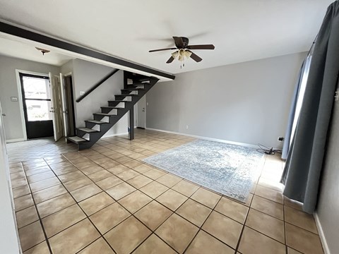 an empty living room with a ceiling fan and a staircase