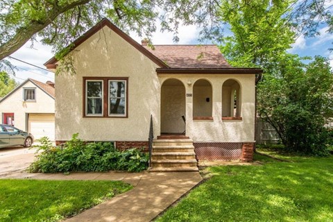 a small tan house with stairs in front of a yard