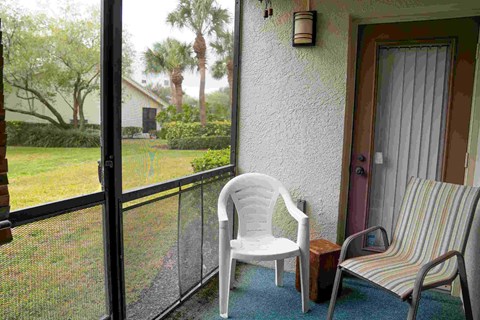 A white plastic chair is on a balcony with a striped metal chair on the porch.