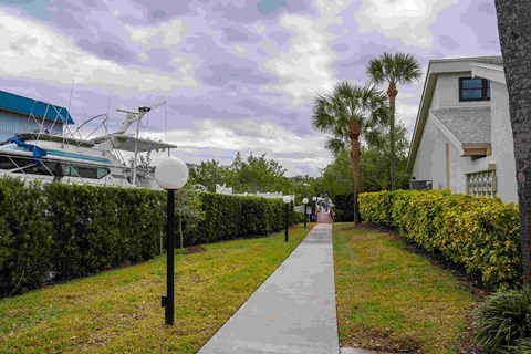 A pathway leads through a well-manicured garden with a yacht and house in the background.