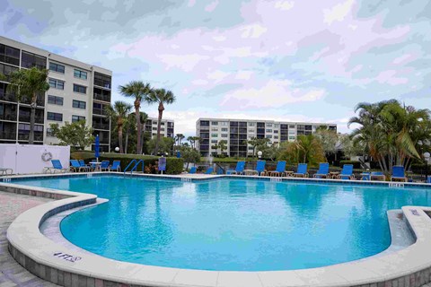 A swimming pool in front of a building with palm trees.