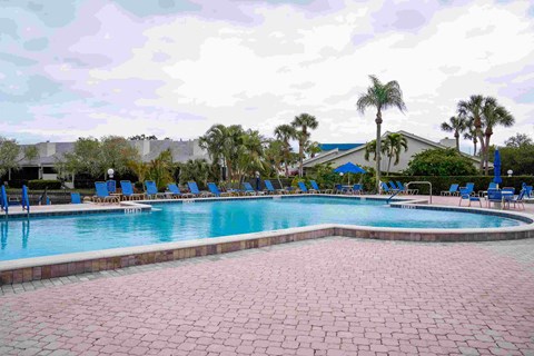 A large swimming pool surrounded by a brick patio and lounge chairs.