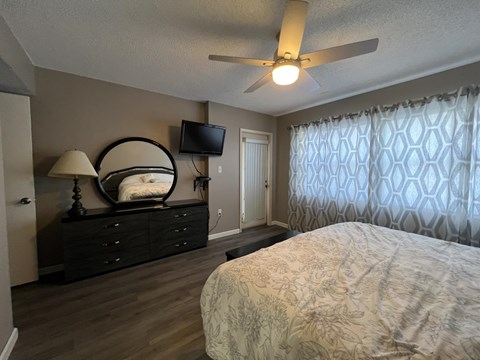 A bedroom with a bed, a dresser, a mirror, a ceiling fan, and a television.