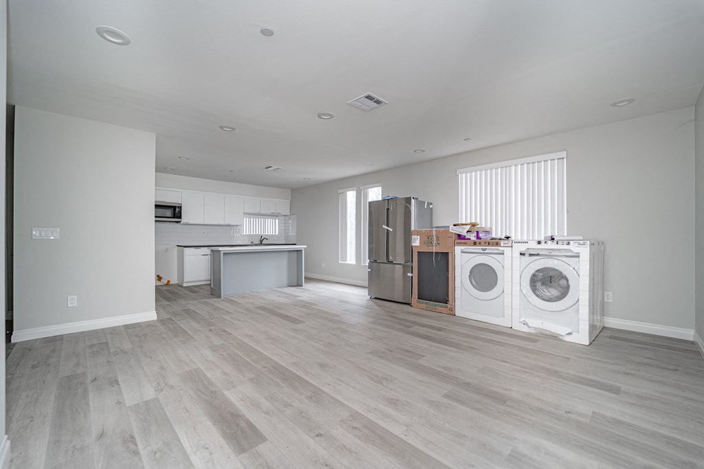 an empty living room with a washing machine and a kitchen