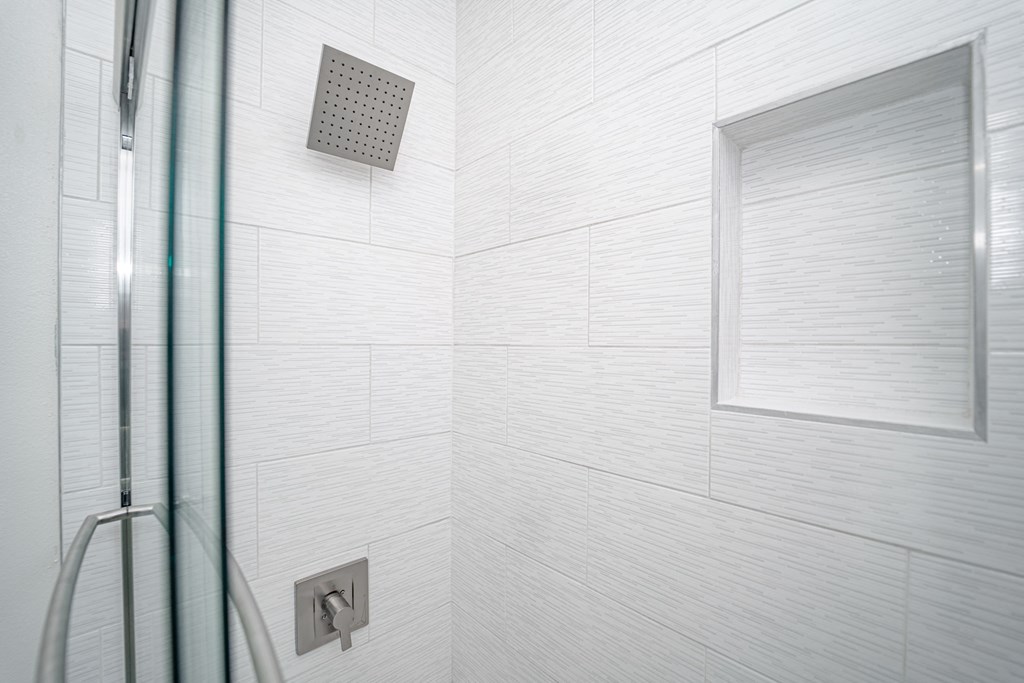a white tiled bathroom with a shower and a window