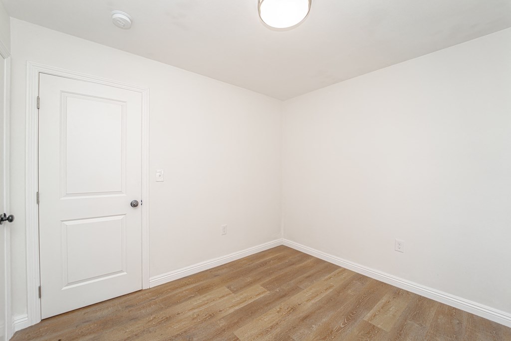 a bedroom with white walls and wood flooring and a white door