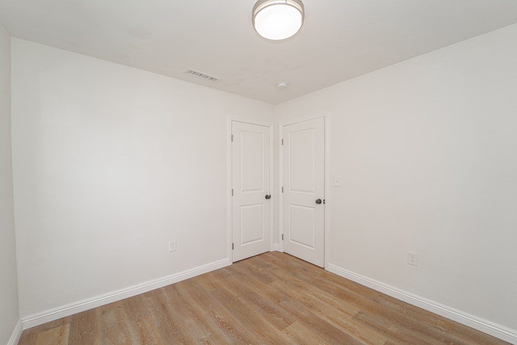 a bedroom with white walls and wood flooring and two doors