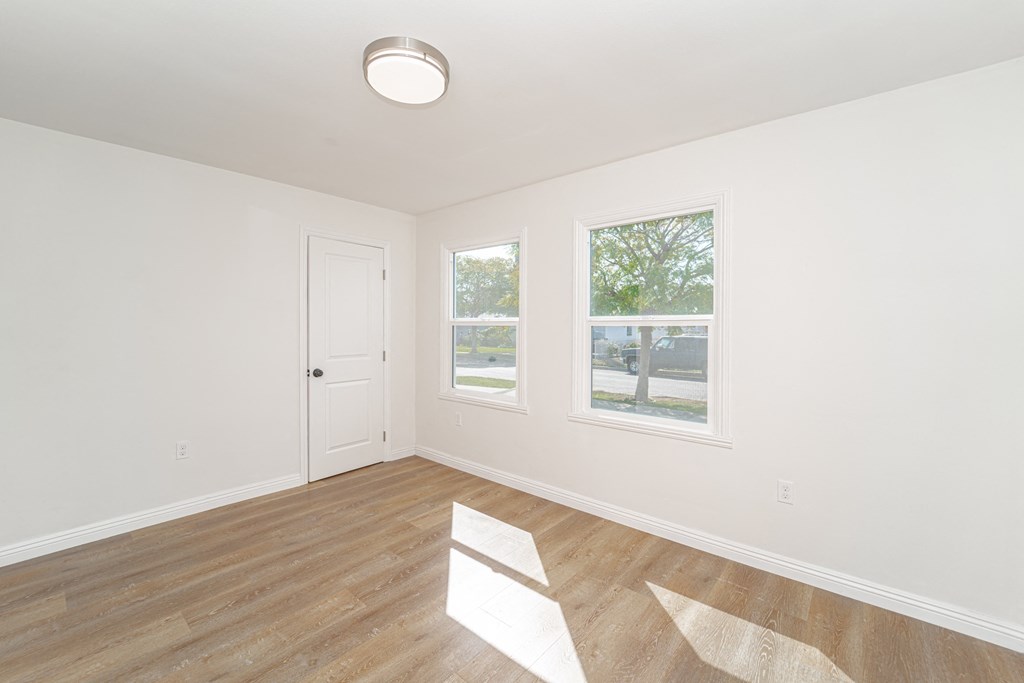 an empty living room with a door and two windows