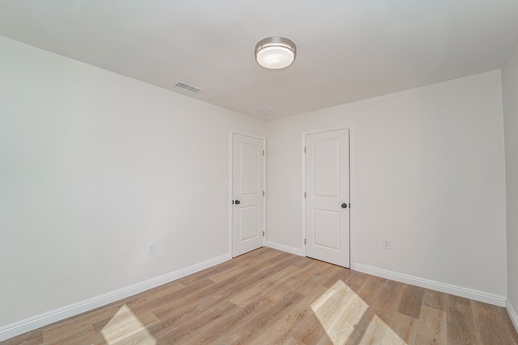 a bedroom with white walls and wood flooring and two doors