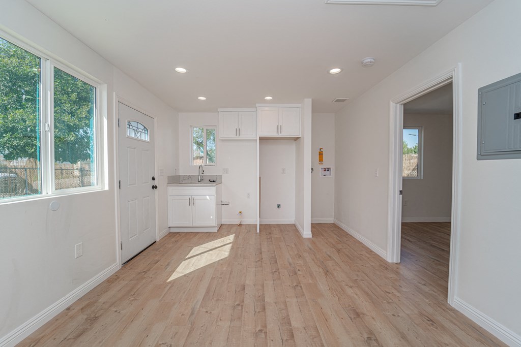 a living room with white walls and a kitchen with wood floors