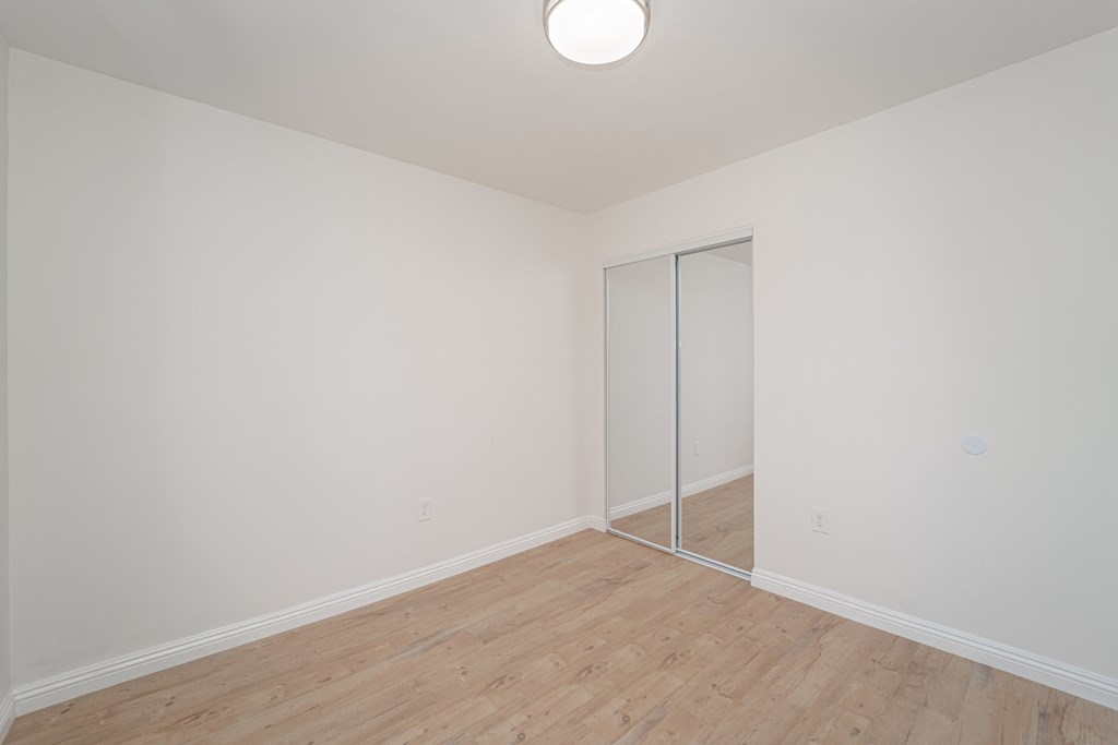 a bedroom with white walls and a wood floor and a mirrored closet