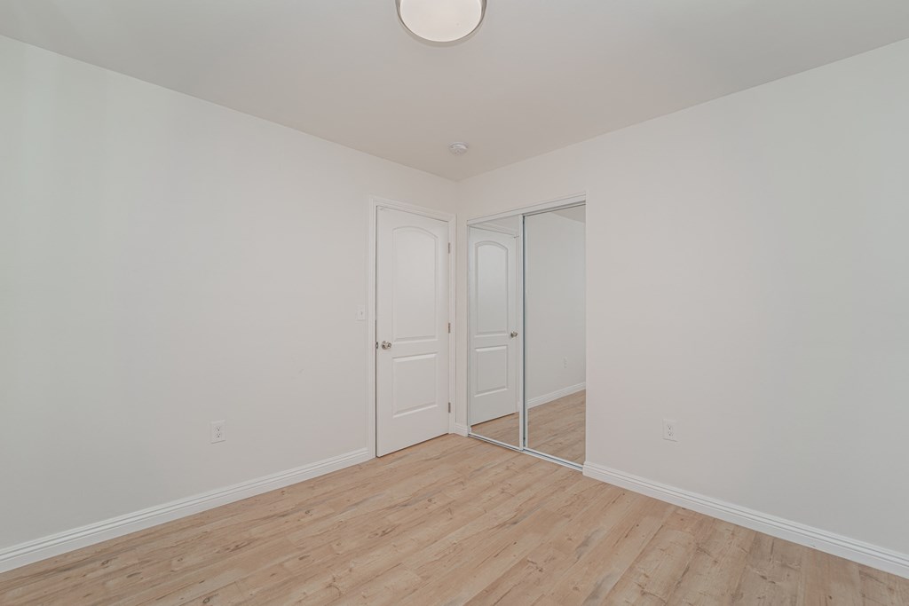 a bedroom with white walls and wood floors and a mirrored closet