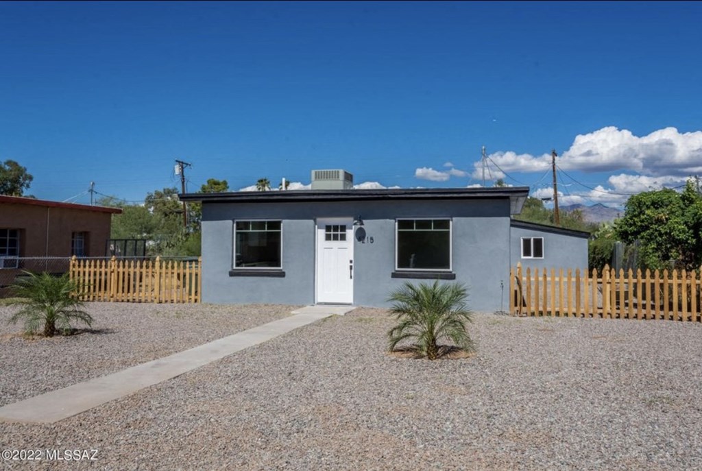 a small white house with a gravel yard and a wooden fence