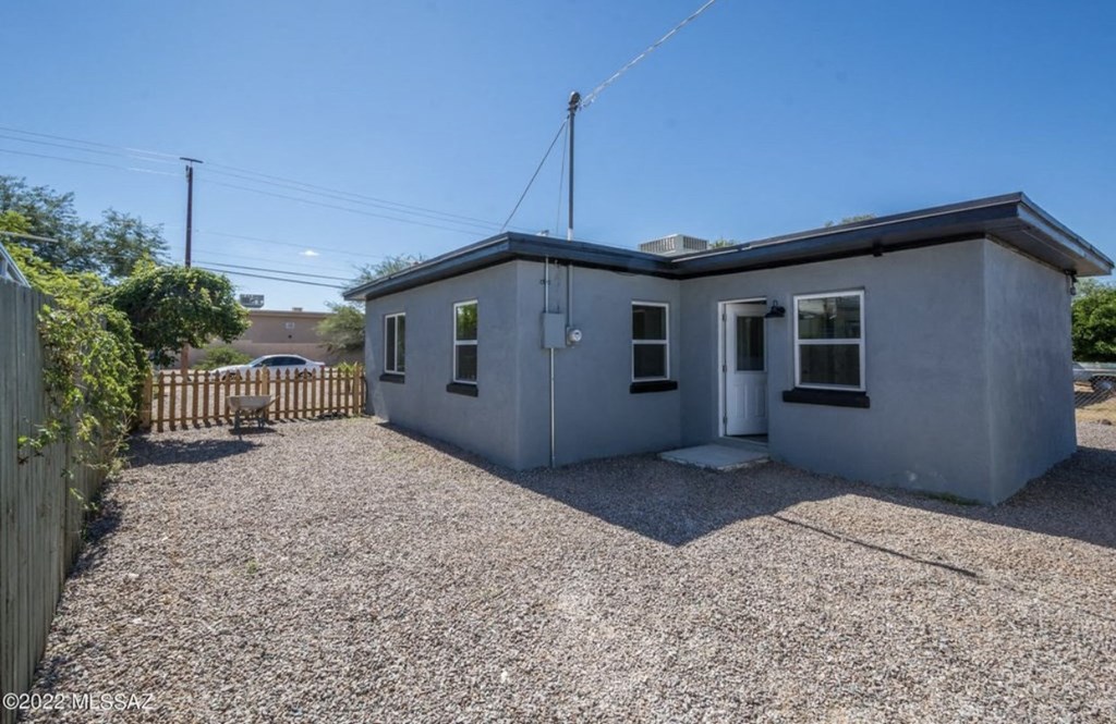 a small gray house with a gravel yard and a fence