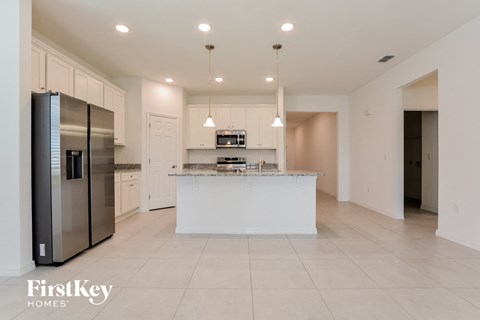 a white kitchen with a large island and stainless steel refrigerator