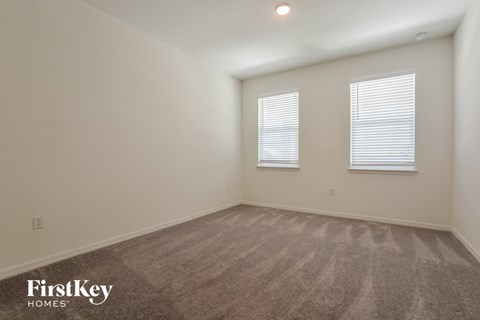 the living room of an apartment with carpet and two windows
