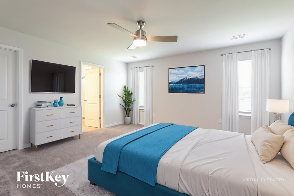 A bedroom with a blue and white bed, a ceiling fan, and a painting on the wall.