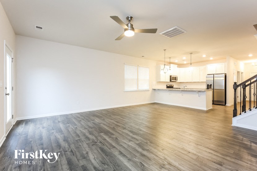 an empty living room and kitchen with wood flooring and a ceiling fan