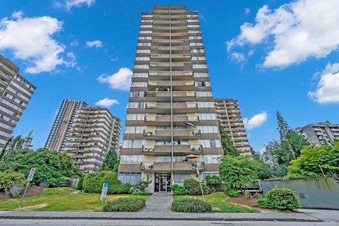 A tall residential building with a green lawn in front.