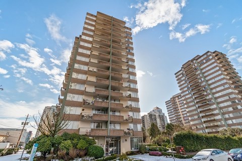 A tall residential building with a parking lot in front.