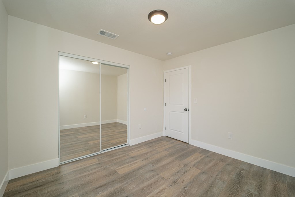 a bedroom with a mirrored closet and hardwood flooring