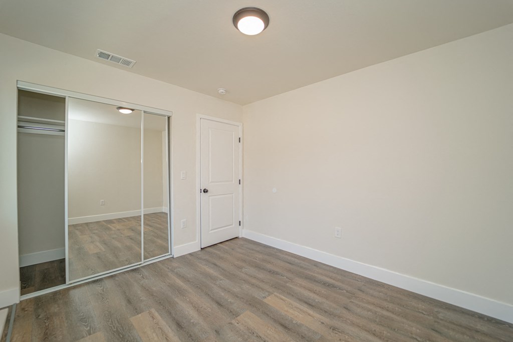 an empty living room with a mirrored closet and wood flooring