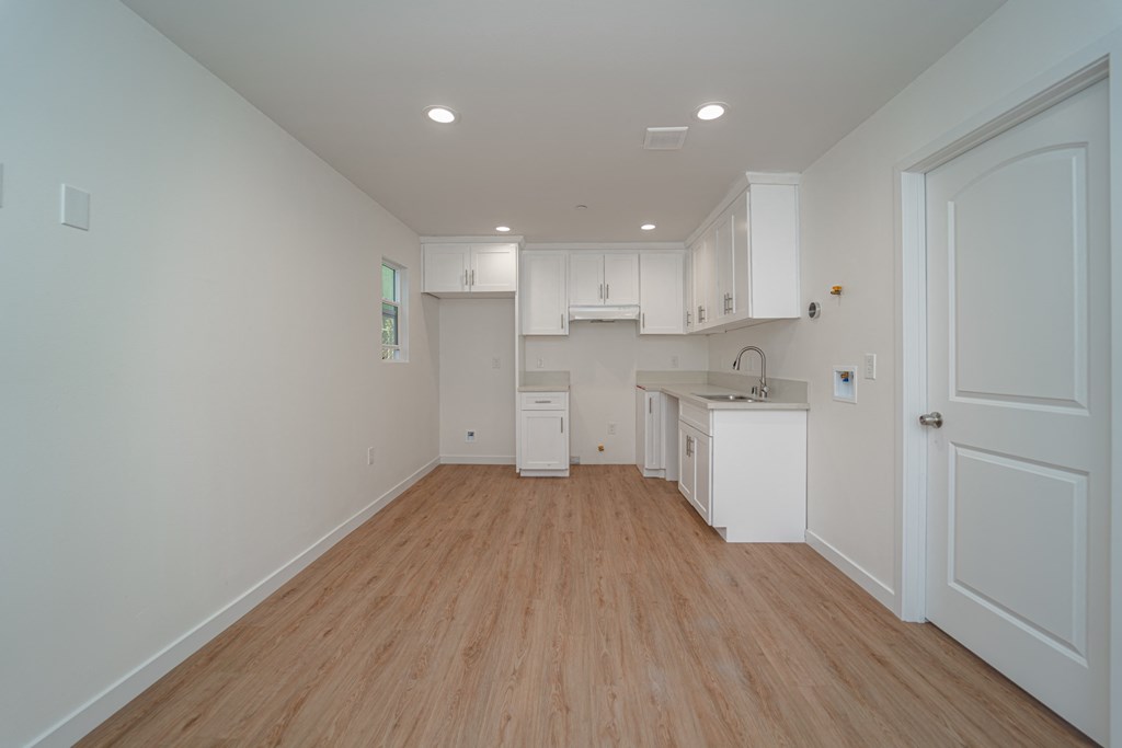 a living room and kitchen with white cabinets and a wooden floor