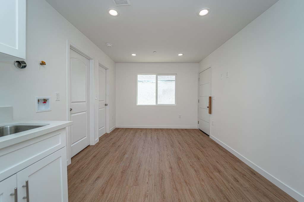a kitchen with white cabinets and white walls and wood floors