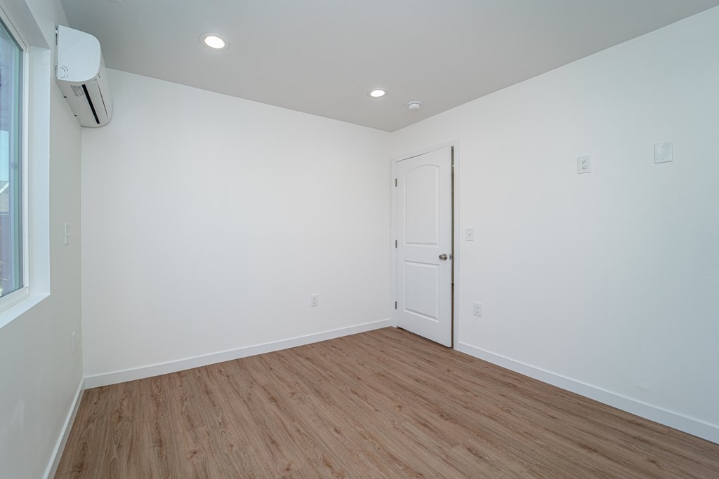 a bedroom with white walls and wood flooring and a door