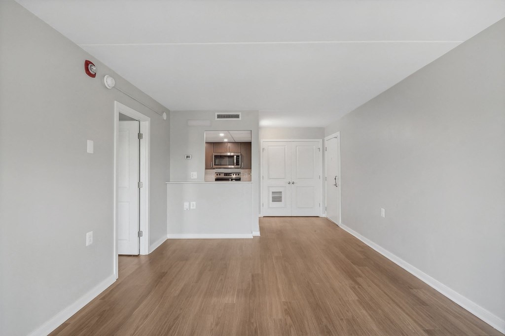 the living room and kitchen of an apartment with white walls and wood floors